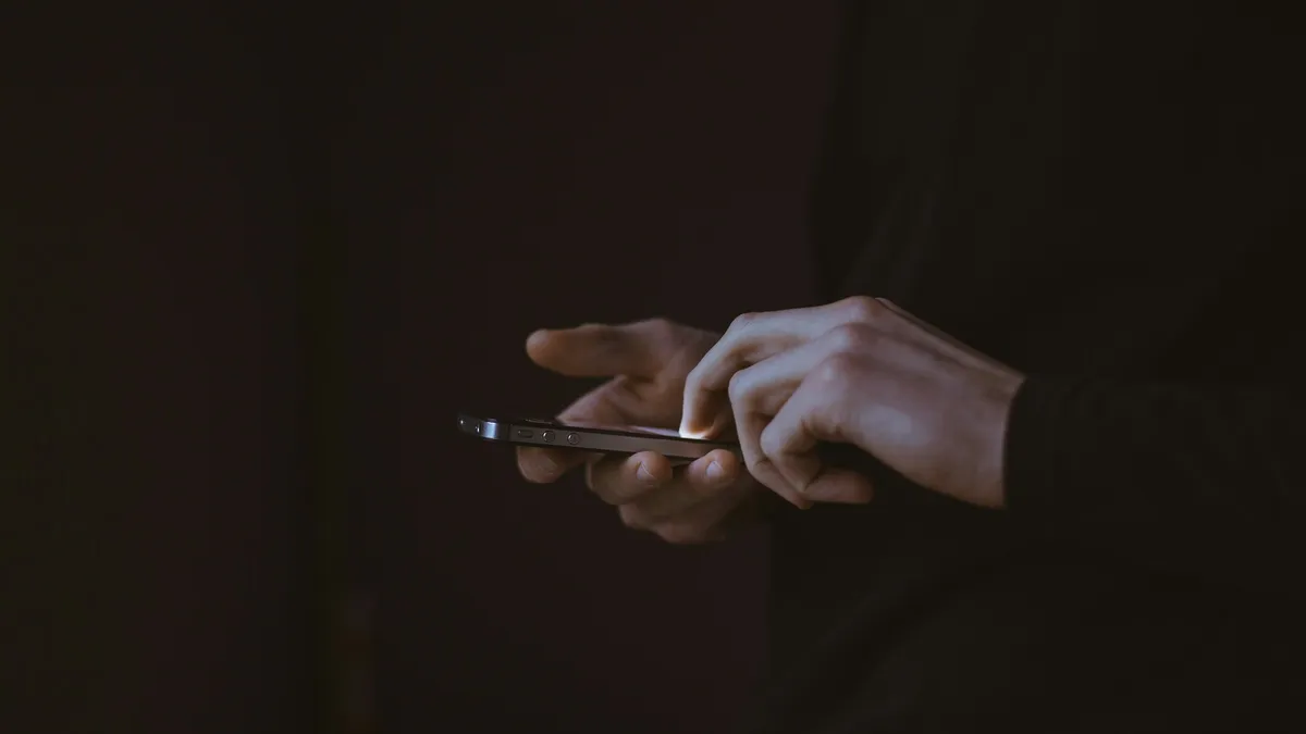 A person's hands hold a lit smartphone in a dark room.