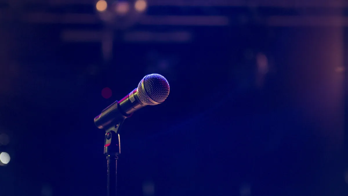 A microphone on a stand, lit against a dark, empty stage.