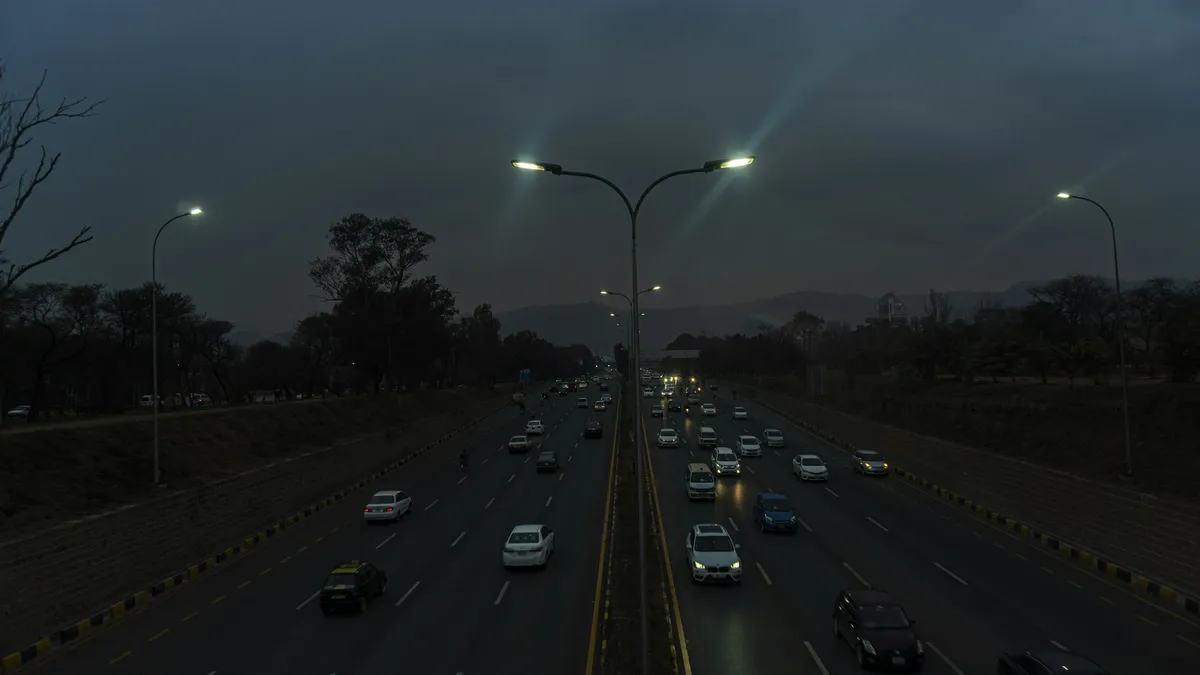 Evening traffic on a divided highway, street lights on, hills in the distance.