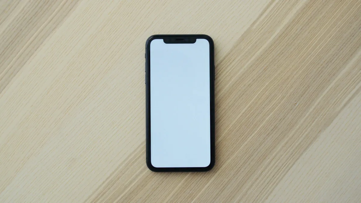 A smartphone with a blank screen lying on a light wooden table.