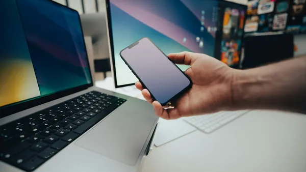 A person holding a cell phone next to a laptop.
