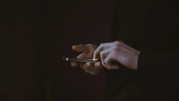 A person's hands hold a lit smartphone in a dark room.