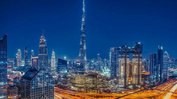 The Dubai skyline at night, with the Burj Khalifa above lit office towers and highways.