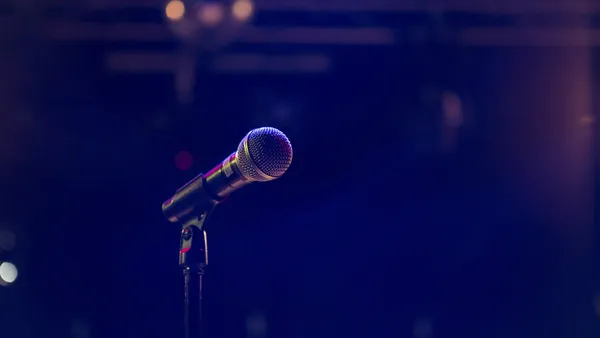A microphone on a stand, lit against a dark, empty stage.