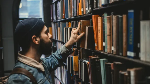 A man reaching for a book on a library shelf.