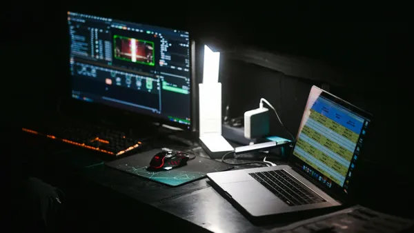 An empty desk at night with a monitor and an open laptop lit up.