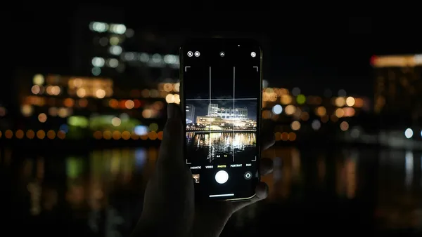 A hand holds up a smartphone against blurred city lights at night.